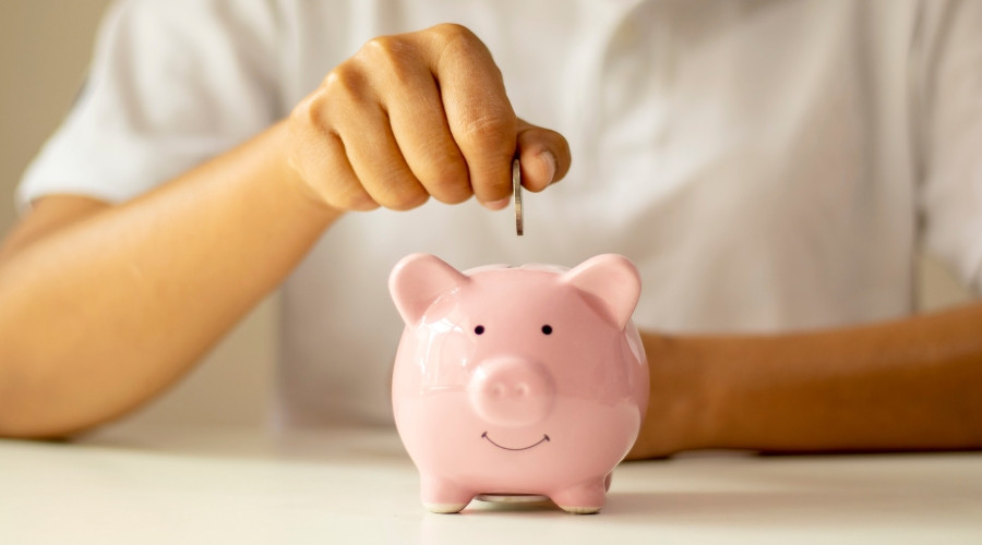 Person inserting a coin into a pink piggy bank, symbolizing saving money and financial efficiency related to cooling cost tips.